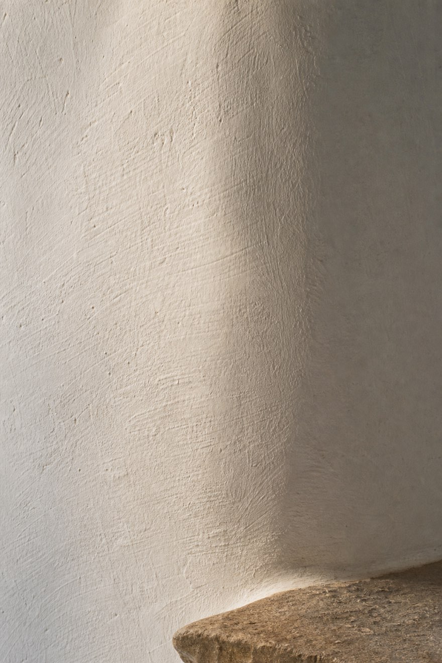 Close-up of hand-troweled white plaster wall texture in soft raking Mediterranean morning light